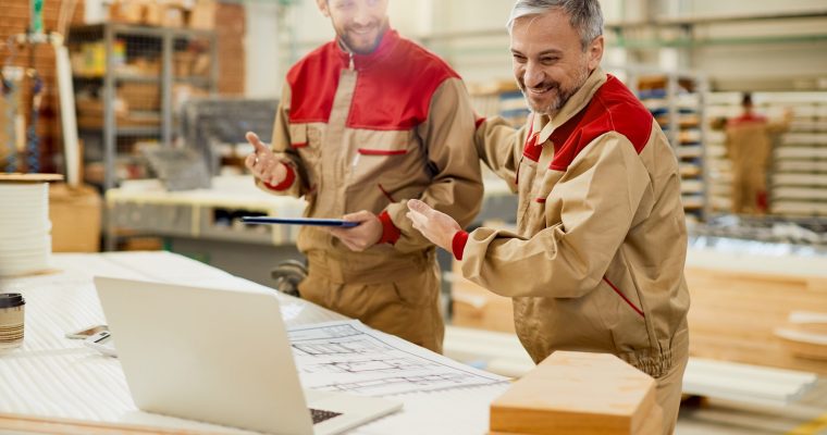 Happy worker and his colleagues using laptop during video call from carpentry workshop.